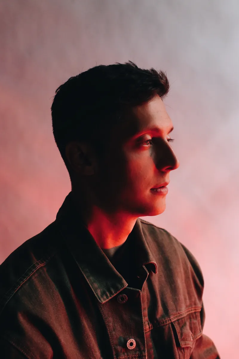 Portrait of Evan Luza in profile, wearing a dark jacket, lit in warm red light